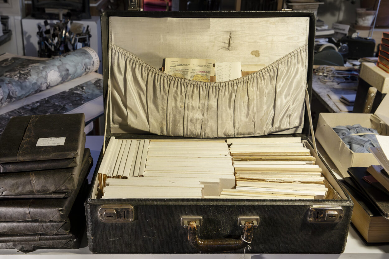 En koffert med gulnat foder fylld med böcker i samma färgton. Fotografi.