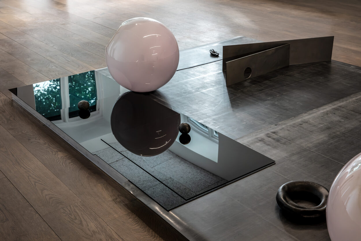 Skulptur på golvet med svarta blanka skivor och ljusrosa glasglob